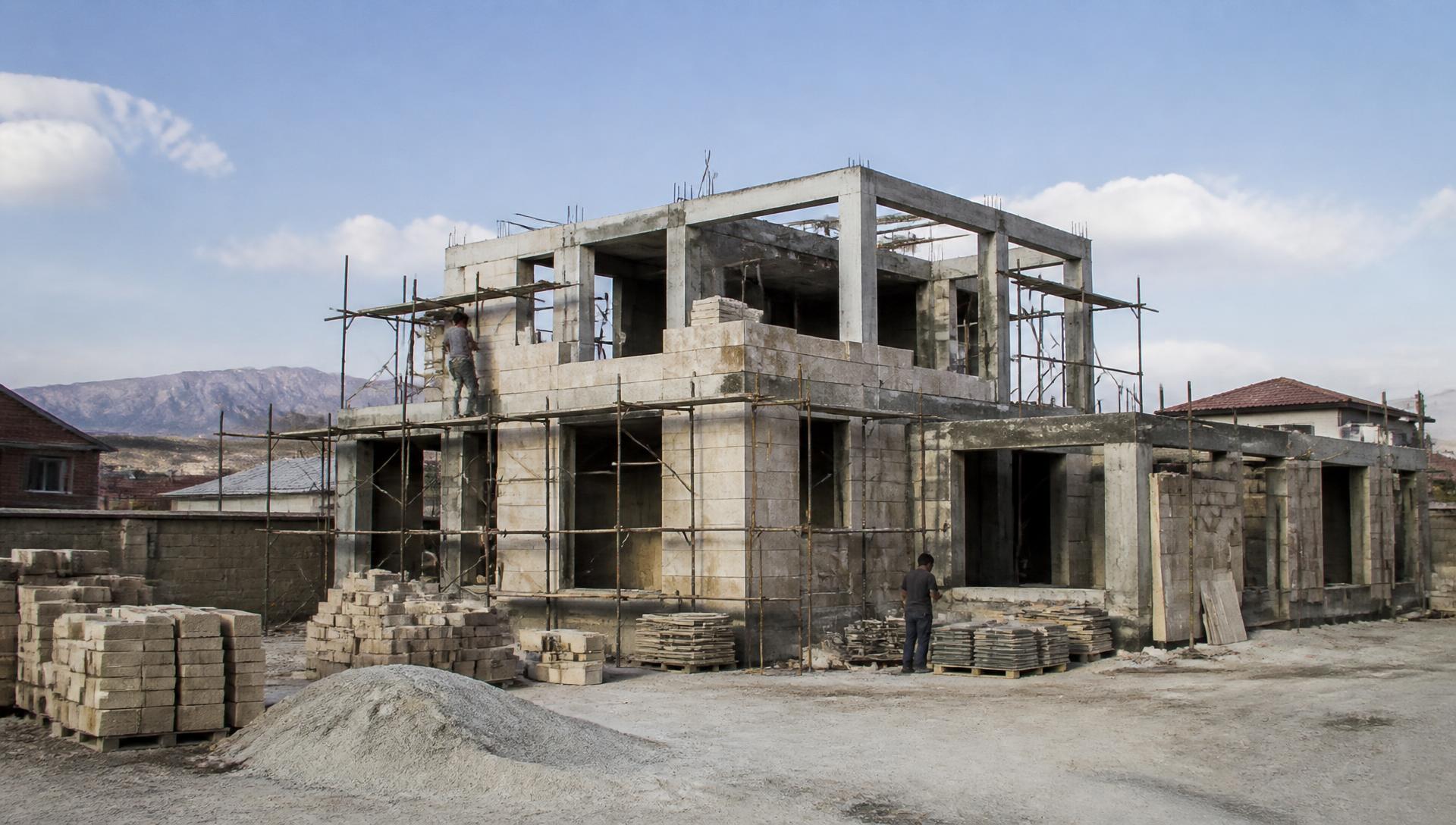 Two-story Armenian house under construction with scaffolding and tuff blocks